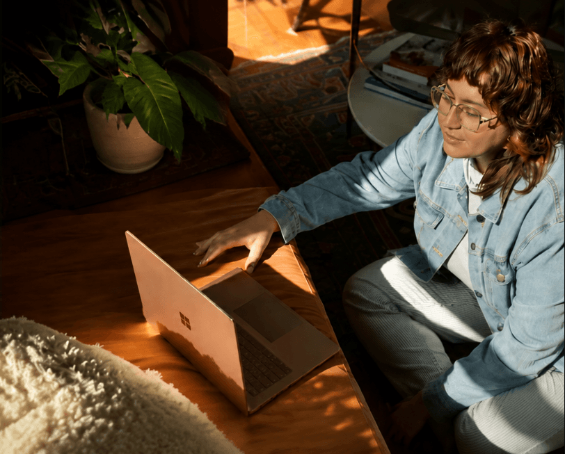 A person at a laptop on the floor of a warmly lit living room, a plant beside them.